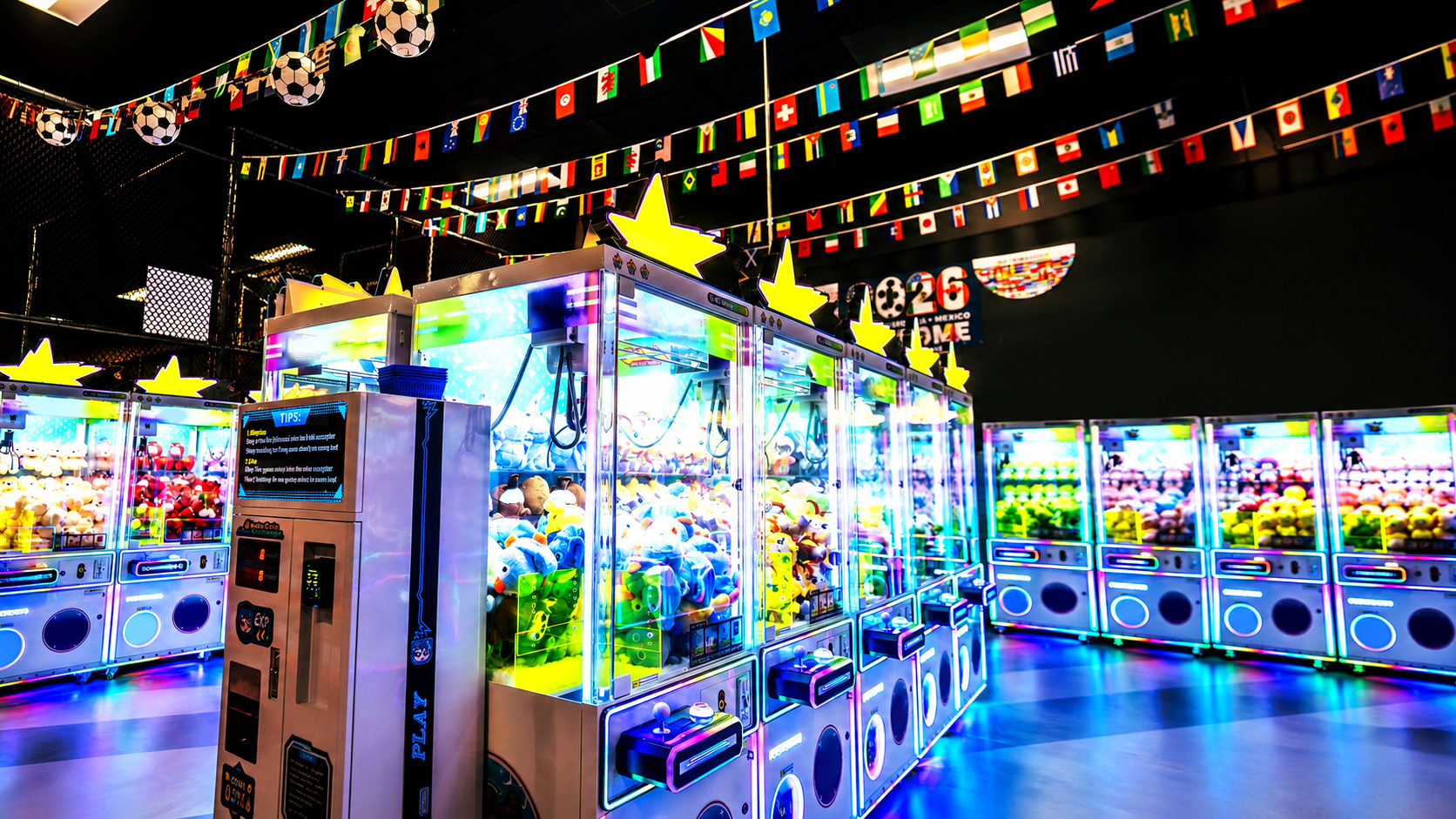 A row of premium commercial claw machines with LED lighting in a modern indoor fun park