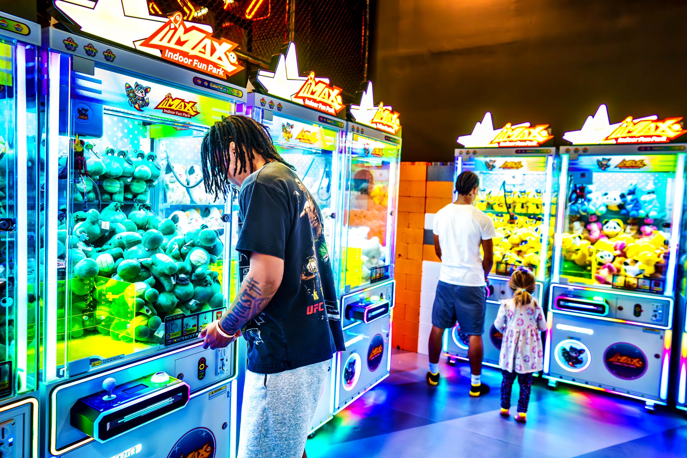 Guests playing at a wall of glowing claw machines inside a busy family entertainment center